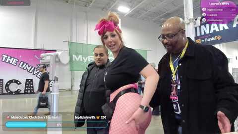 Media: Video of a vibrant convention scene featuring a woman in a pink wig and high-waisted pants, flanked by two men, all smiling.