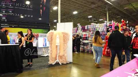 Media: Video of a bustling trade show with a model in a beige dress, people in casual attire, and colorful display stands.