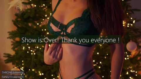 Media: A video of a slender, light-skinned woman in green lace lingerie, standing in front of a warmly lit Christmas tree. Text overlay: \"Show is Over! Thank you everyone!\