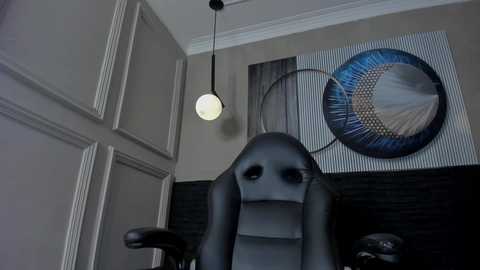 Media: A video of a large, black, humanoid chair with a round, glowing headlight, in a modern room with a striped wall and abstract art.