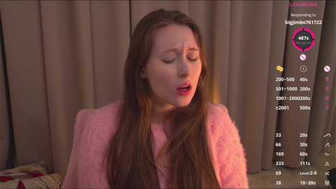 Video of a fair-skinned woman with long brown hair, wearing a pink fuzzy sweater, looking distressed with eyes closed and mouth open, surrounded by a live-streaming interface.