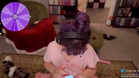 A video shows a person with purple hair, wearing a VR headset, playing a game on a carpeted floor with a purple stream overlay.