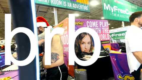 Media: Video of a bustling computer convention with attendees wearing Santa hats, holding colorful banners, and a tattooed woman. Background includes green and purple promotional signs.