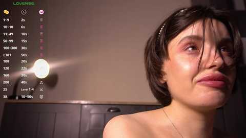 Media: A video of a young woman with fair skin, dark hair, and freckles, wearing a white headband, captured in a dimly lit room.