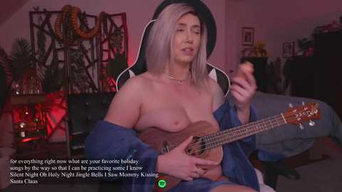 Media: Video of a topless, light-skinned woman with long, platinum blonde hair, playing an acoustic guitar in a dimly lit, cozy bedroom. Text overlay reads: \"A little late night what your favorite holiday.\