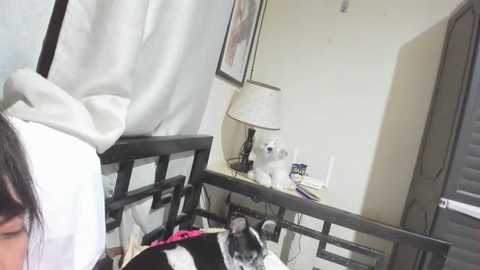 Media: A video of a woman in a white robe, standing beside a black-framed mirror in a bedroom. A black cat with white markings sits on a white bed, surrounded by scattered clothes.