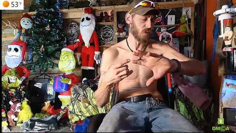 Media: Video of a shirtless, muscular man with a beard and sunglasses, gesturing, in a cluttered room with Halloween decorations, including Jack Skellington and a Santa figure.