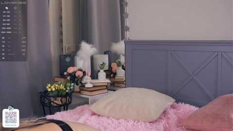 Media: Video of a stylish, modern bedroom with a light gray wall and wainscoting, featuring a white bed with a pink shag rug, a black metal side table with a vase of flowers, and a mirror reflecting the room's decor.