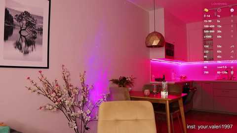 Media: A video of a modern, minimalist living room with a cozy dining area. A pink light illuminates the room, casting a warm glow. The dining table is adorned with a vase of cherry blossoms, and a large wall-mounted clock with a black background and white numbers is visible.