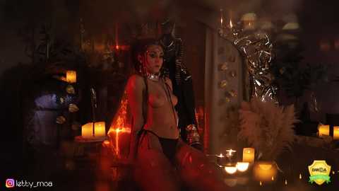 Media: Video of a topless, dark-skinned woman with large breasts, wearing only black panties, kneeling in a dimly lit, candle-lit room with a metallic skeleton and a witch hat.