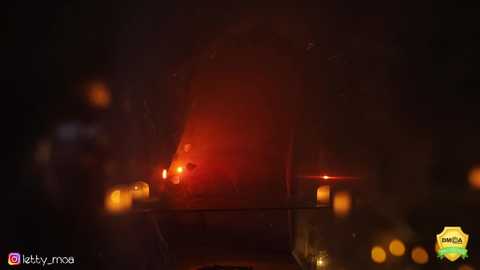 Media: Video of a dark, smoky night scene with a bright red car light in the foreground, surrounded by dimly lit candles and blurred bokeh lights in the background.