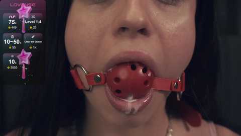 Media: Video of an Asian woman with long black hair, wearing a red ball gag and a red leather collar, with a digital game interface overlay displaying health and stamina bars.