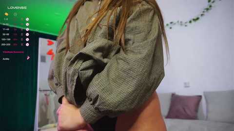 Media: Video of a woman in a green knit sweater, partially lifting it to reveal her bare chest, in a bedroom with a bed, wall art, and green lighting.