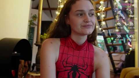 Media: Video of a young woman with fair skin and long brown hair, wearing a red Spider-Man costume, indoors with a spiral staircase and fairy lights in the background.