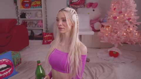 Media: Video of a blonde woman in a purple off-the-shoulder crop top, holding a champagne bottle in a cozy, festive living room with a pink Christmas tree and wrapped gifts.