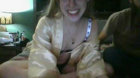 Media: A dimly-lit video shows a smiling young woman with blonde hair, wearing a satin robe, in a bedroom setting. A man's hand is visible, partially covering her breast.