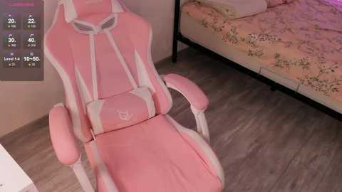 Video of a pink gaming chair with white accents and a floral-patterned bed in a cozy bedroom with wooden flooring.