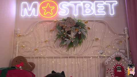 Media: A video of a whimsical, festive bedroom featuring a white metal bed adorned with a starry garland, a \"MOSCOW\" neon sign, and holiday decorations including a plush bear and candy cane.