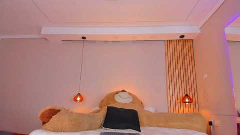 Media: A video of a cozy bedroom with a plush teddy bear headboard, two hanging red pendant lights, and warm ambient lighting.