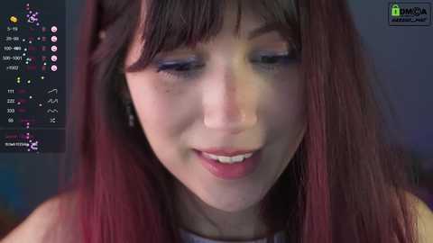 Media: Video of a young woman with long, dark brown hair, wearing a black top, smiling. The background is blurred with a chat interface visible.