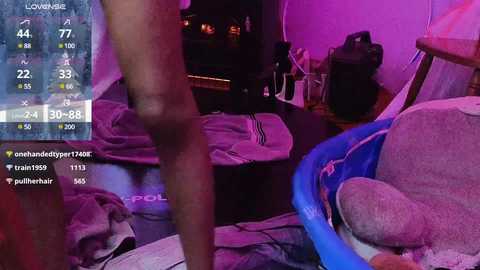 Media: Video of a dimly lit room with purple lighting, featuring a man's naked lower body standing, a disheveled bed, and a blue chair, with a live stream overlay displaying temperature and location data.