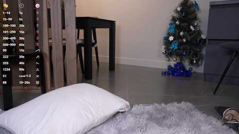 Media: A video of a modern living room with a cozy, light gray rug, a fluffy white pillow, a black dining table, a decorated Christmas tree, and a blue and silver garland.