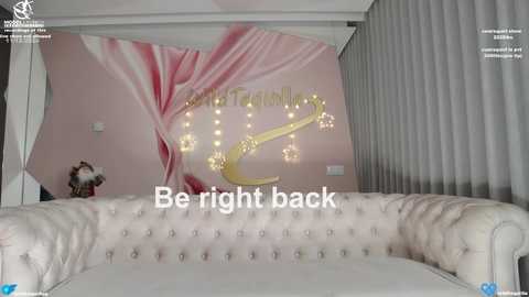 Media: Video of a luxurious living room featuring a tufted white sofa, a pink and white abstract mural, and a \"Be Right Back\" message on a digital screen.