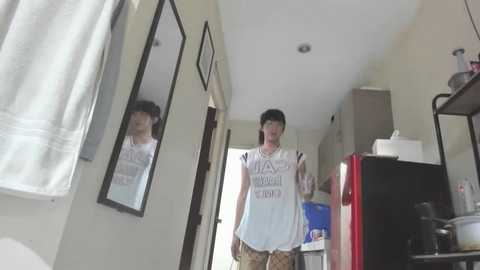 Media: Video of a person with short black hair, wearing a white \"I'M NOT A DOCTOR\" shirt, standing in a brightly lit, cluttered kitchen with beige walls and a red fridge.