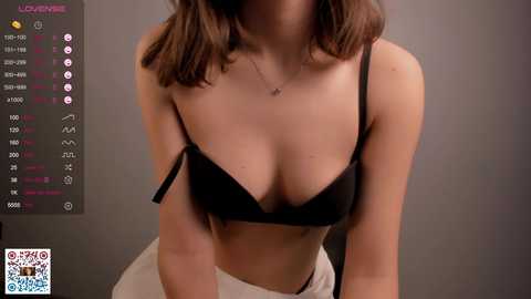 Video of a fair-skinned woman with shoulder-length brown hair, wearing a black bra and white pants, against a grey background.