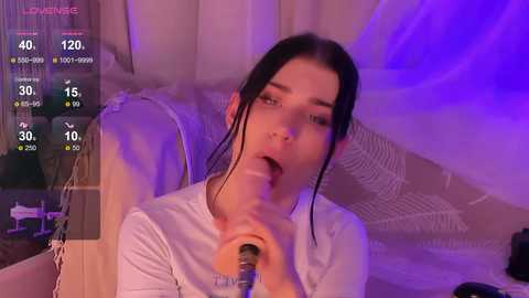 Media: Video of a young woman with fair skin, dark hair, wearing a white shirt, holding a realistic, life-sized dildo, in a dimly lit room with purple lighting, and a virtual reality headset.