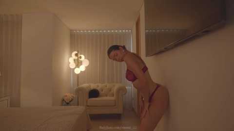 Media: A video shows a slender, light-skinned woman in red lingerie, leaning against a wall in a dimly lit living room with beige curtains, a cream sofa, and a decorative lamp.