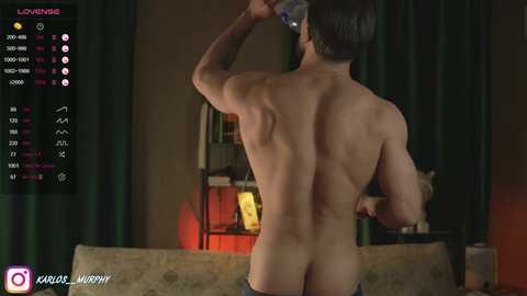 Media: Video of a muscular, shirtless man with short dark hair, facing away, pouring a drink. Background shows dimly lit room with green curtains and bookshelves.