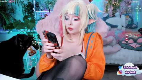 Media: A young woman with blonde hair and elf ears in cosplay attire, orange jacket, and black stockings, sitting indoors, playing with a black cat, surrounded by plants and posters.