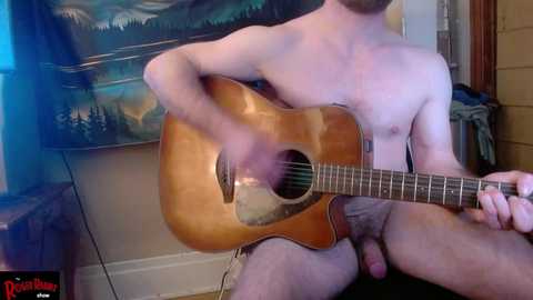 Media: Video of a shirtless man with a medium build, playing an acoustic guitar with a visible erection. Background features a mountain landscape tapestry and wooden walls.