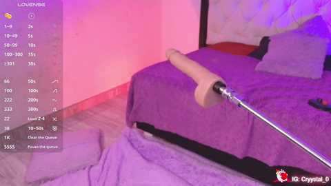 Media: A video of a purple bed with a wooden dildo on a silver stand, set against a pink wall with a mirror, taken from a first-person POV.