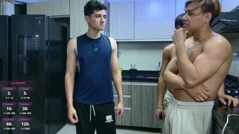 Media: Video of three shirtless men in a modern kitchen: one in a dark blue sleeveless shirt, another in white shorts, and the third in gray shorts, with a digital display showing temperature and time.