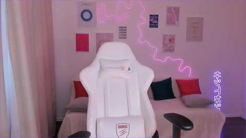 Media: Video of a modern gaming setup featuring a white gaming chair, a beige sofa with red and blue pillows, and a wall adorned with colorful posters and neon lights.