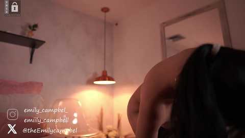 Video of a dimly lit, cozy bedroom with a red pendant light, a potted plant, and a black headboard, featuring a person with black hair, partially visible, wearing a black top.