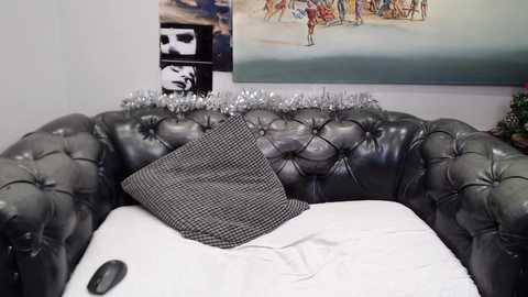 Media: Video of a plush, tufted, dark green leather sofa with a black-and-white checkered pillow, adorned with a festive garland. Background features a large, colorful painting and a black-and-white photo collage.