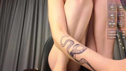 Media: Video of a nude woman with fair skin, sitting on a chair. She has a snake tattoo on her right forearm. Background features dark curtains and digital stats overlay.