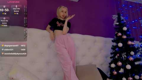 Media: Video of a blonde woman with fair skin, wearing a black crop top and high-waisted pink pants, posing seductively in front of a Christmas tree, with a digital overlay showing her Discord chat.