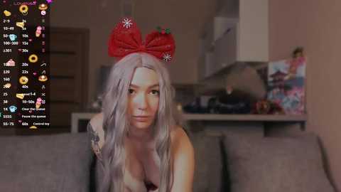 Media: A video of a woman with long, wavy gray hair, wearing a red strawberry headband, sitting on a gray couch. The background shows a dimly lit kitchen.