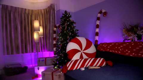 Media: Video of a cozy, festive bedroom with a Christmas tree, a giant candy cane, and a red-and-white-striped pillow. Purple and white lights illuminate the room, creating a warm, holiday ambiance.