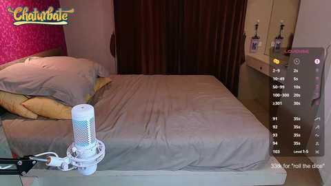 Media: Video of a neatly made bed with beige sheets, a white oscillating fan, and a digital display showing a \"Chlorophyll\" label. Background includes a pink floral-patterned wall and a wooden nightstand with two bottles.