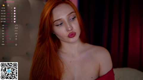 Media: Video of a pale-skinned woman with long, vibrant red hair, wearing red lipstick, and a red off-shoulder top. Background features dark curtains.