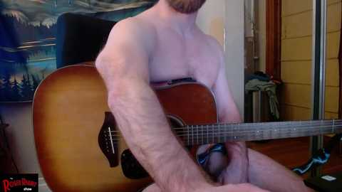 Media: A video shows a shirtless man with a beard, playing an acoustic guitar indoors. The background features a framed landscape painting and a wooden door.