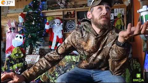 Media: Video of a bearded man in a camo jacket and cap, gesturing excitedly at a festive display featuring Santa, skeletons, and a green alien. Background includes wooden shelves and holiday decorations.