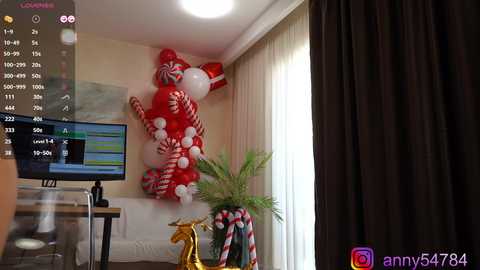 Media: Video of a cozy living room with a red, candy-themed Christmas decoration, a TV displaying a streaming platform, and a gold reindeer figurine on a white couch.