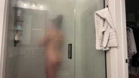 Media: A blurred video of a nude woman with long, dark hair in a glass shower, holding a white towel, with toiletries visible in the background.