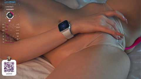 Media: Video of a light-skinned woman with a slim physique lying on her back, wearing a white sports bra and a smartwatch. Her hand rests on her stomach, with a barcode and \"Kino\" watermark in the bottom left corner.